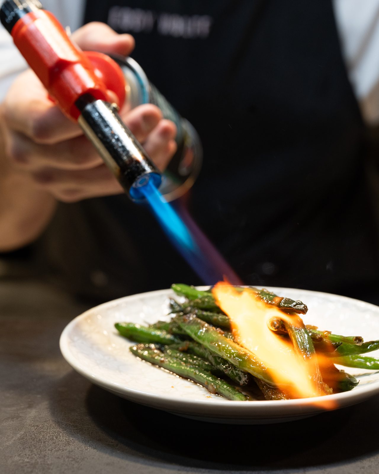 A plated dish on the pass at Eddy + Wolff, with the open kitchen behind it