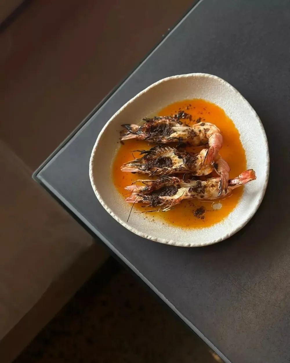 Four charcoal-grilled shrimp in a vibrant orange sauce at Eddy + Wolff—a signature 100% Gluten-Free Southeast Asian seafood dish.