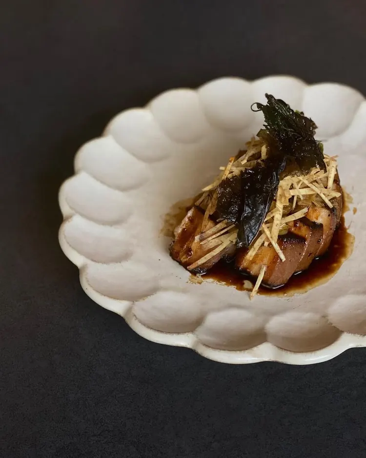 Lap yuk pork belly with a glossy dark sauce, topped with crisp shredded garnish and nori, on a scalloped white plate